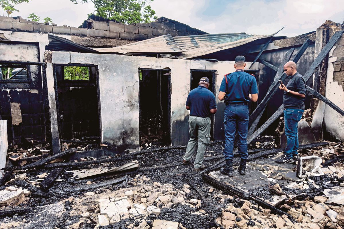 PASUKAN penyiasat dan kakitangan kerajaan memeriksa bangunan asrama yang musnah akibat kebakaran berkenaan. FOTO AFP