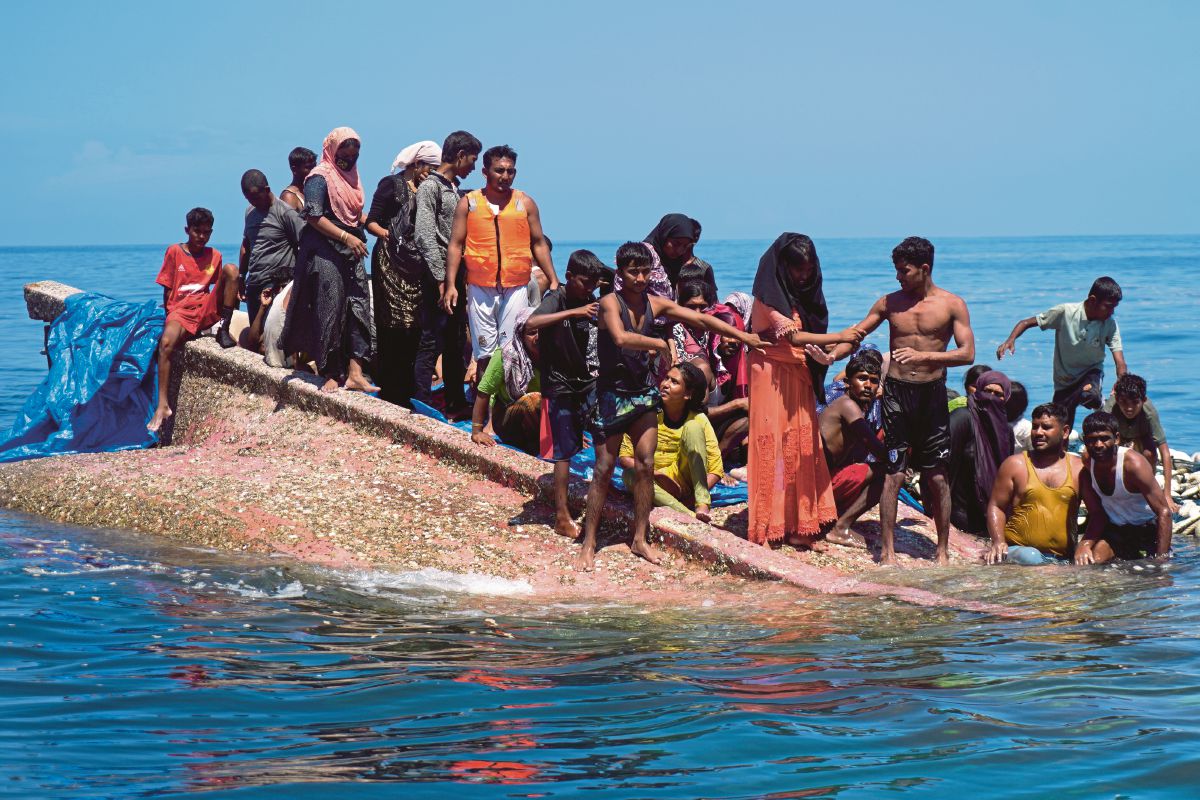 PELARIAN Rohingya duduk di atas badan bot yang terbalik di luar pantai barat Aceh. FOTO Reuters