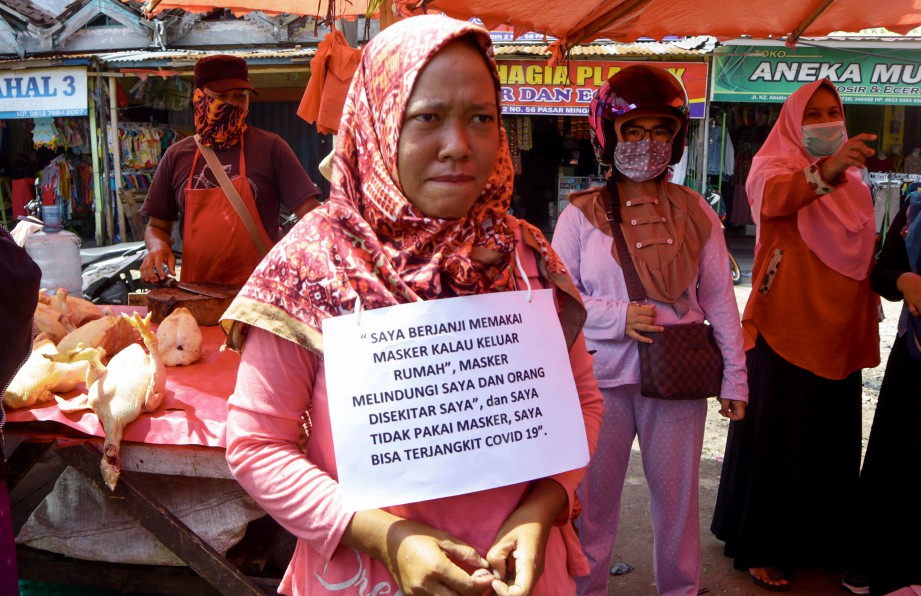 WANITA dihukum menggantung plakad akujanji di leher selepas ditemui tidak memakai pelitup muka di Bengkulu. FOTO AFP