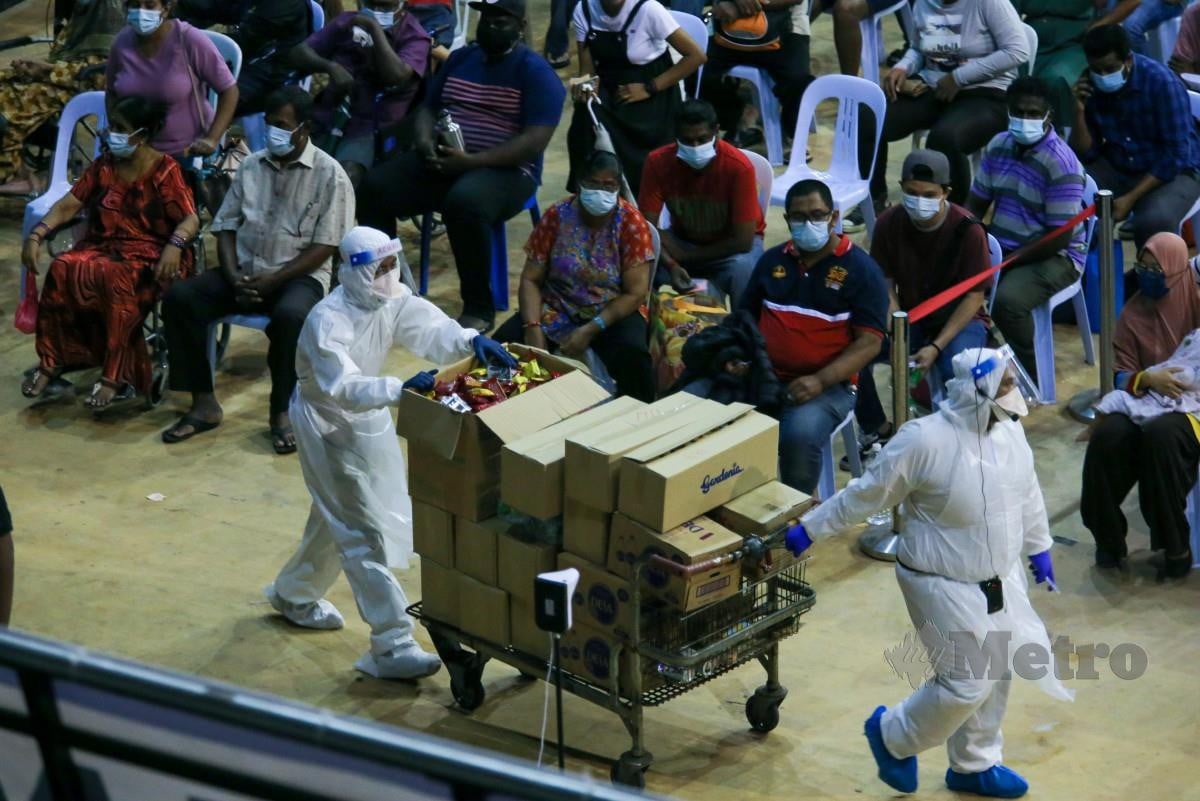 PETUGAS membawa makanan untuk diagihkan kepada orang ramai di Pusat Penilaian Covid-10 (CAC) Stadium Melawati, Shah. FOTO Aswadi Alias.