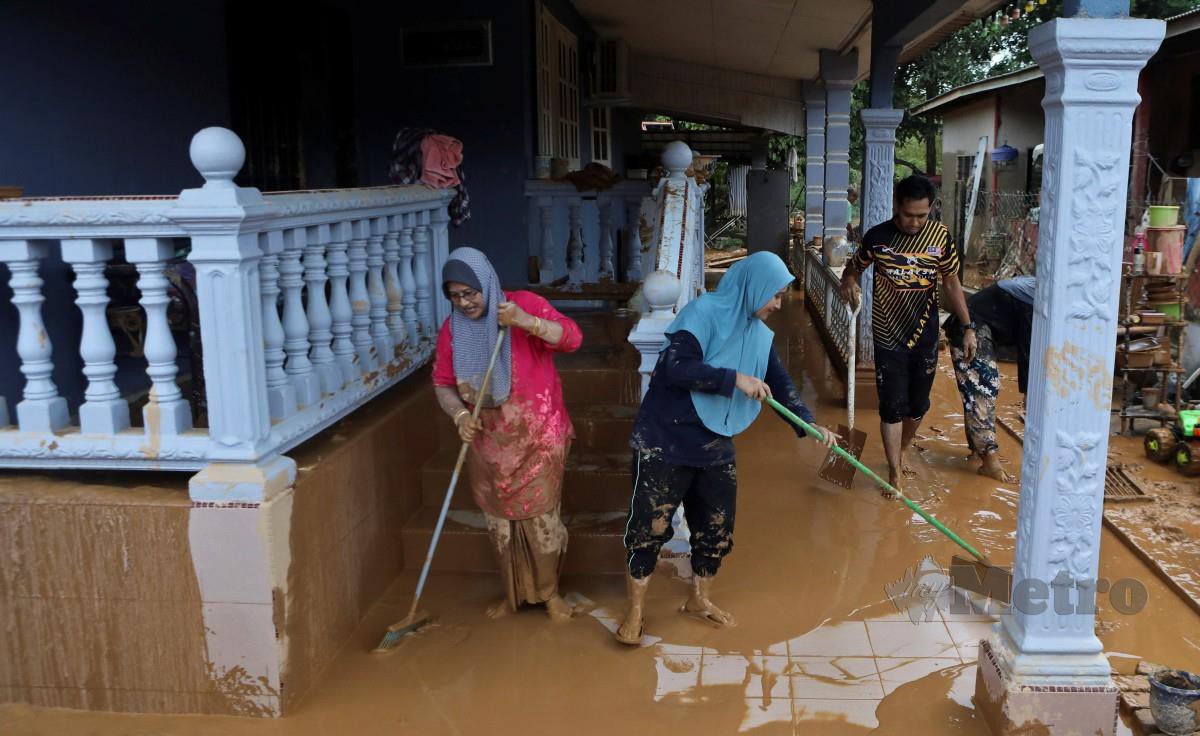 PENDUDUK membersihkan kawasan rumahnya yang dilanda banjir di Kampung Bukit Gemuruh. FOTO Ghazali Kori.