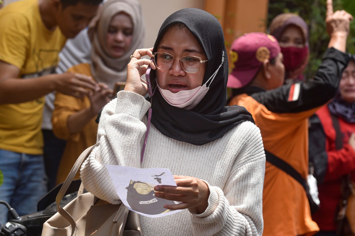 SEORANG wanita menangis sambil membuat panggilan dengan tangannya memegang gambar mangsa kejadian rempuhan di Stadium Kanjuruhan, Malang. FOTO AP