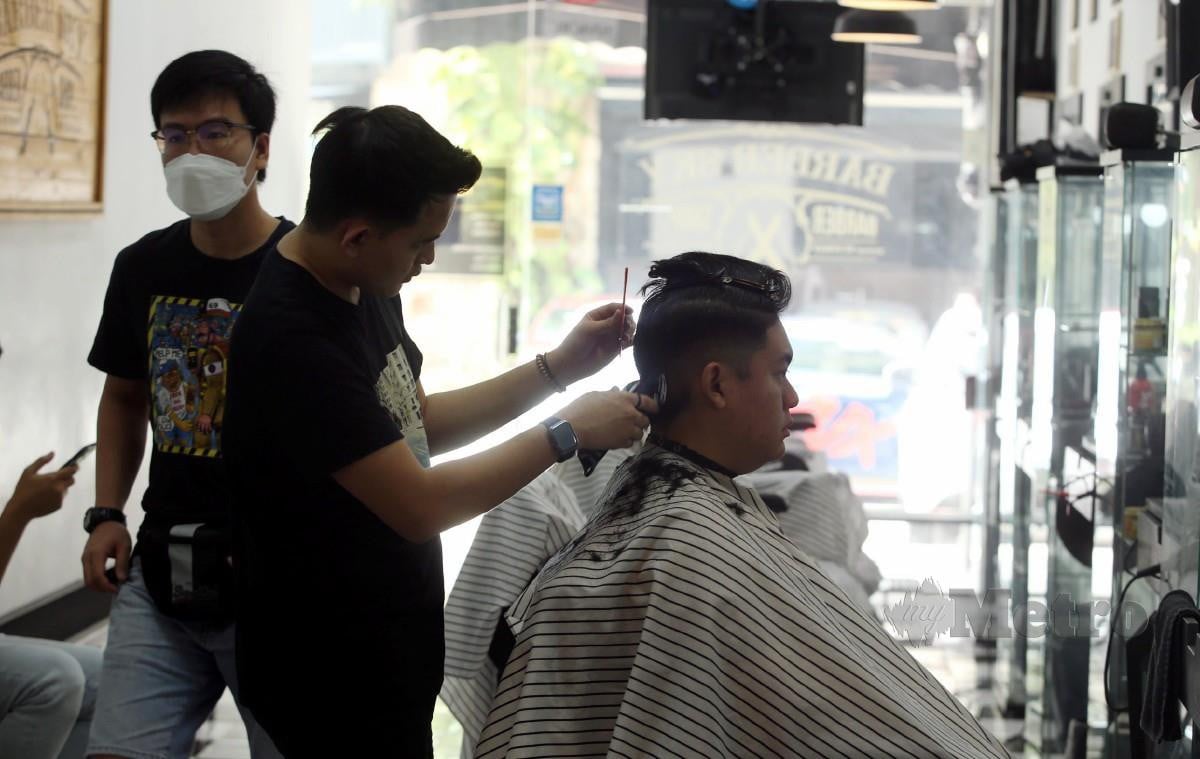 TUKANG gunting rambut, Idzhan Zaqwan Ahmad Saufi menggunting rambut pelanggan. FOTO Hairul Anuar Rahim.