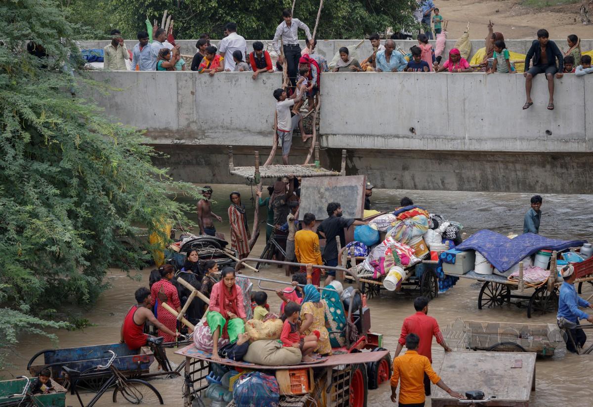 PENDUDUK memanjat ranting pokok bagi memanjat jejambat yang dalam pembinaan sementara menunggu untuk dipindahkan akibat kejadian banjir susulan kenaikan paras air sungai Yamuna. FOTO Reuters