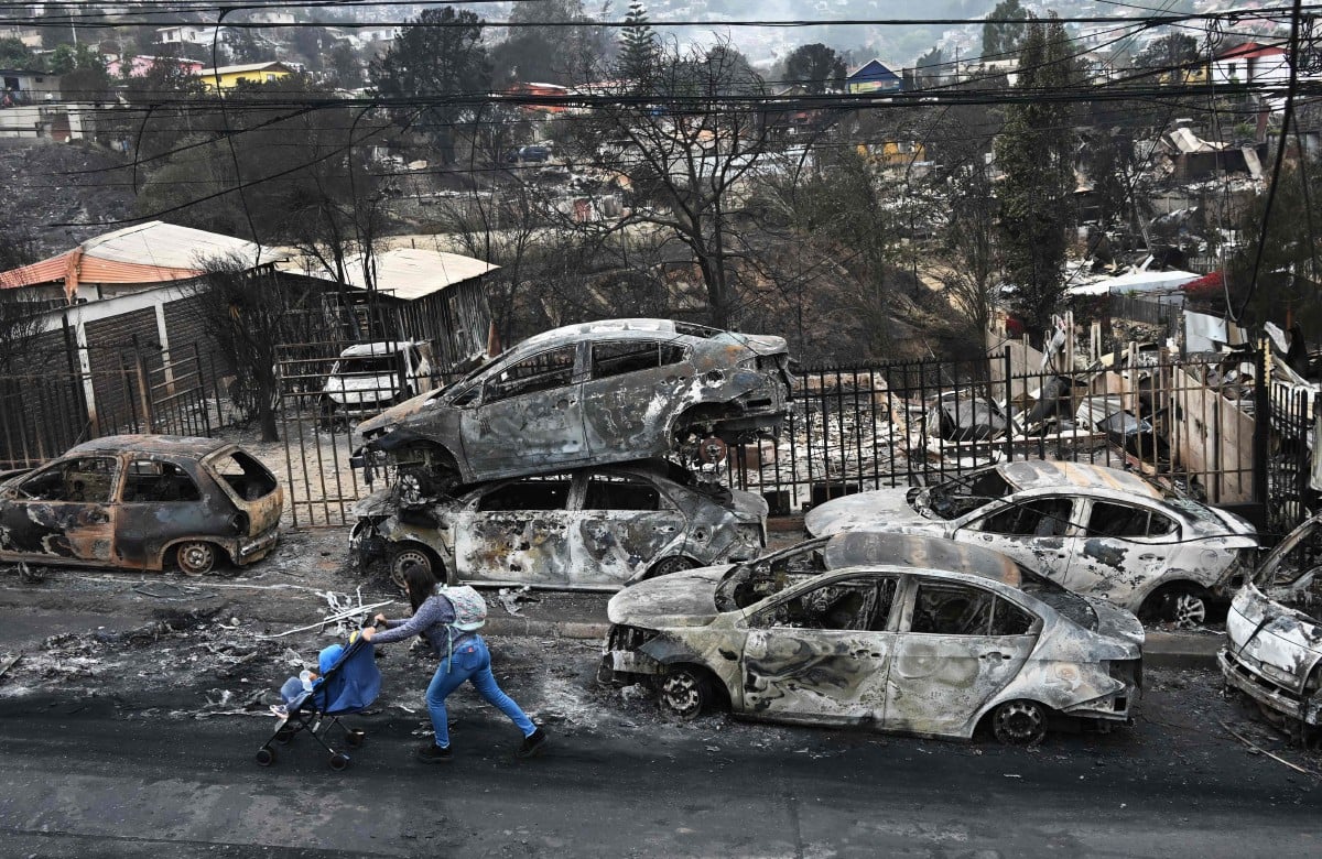 GAMBAR fail menunjukkan seorang wanita melintasi kenderaan yang terbakar di bandar peranginan Vina del Mar, pada Februari lalu. FOTO AFP