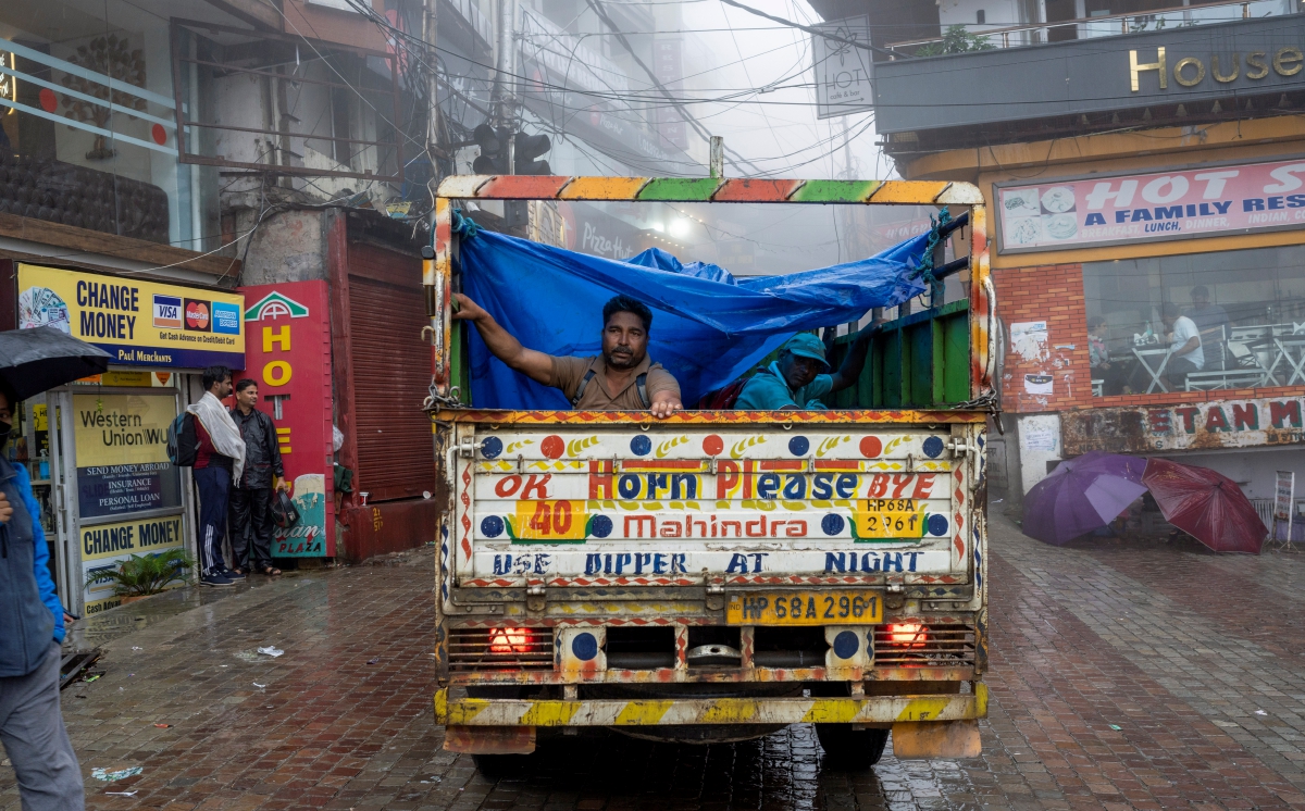 Orang ramai yang menaiki kenderaan terbuka duduk di bawah kain terpal untuk berlindung daripada hujan di Dharmsala, India. FOTO AP