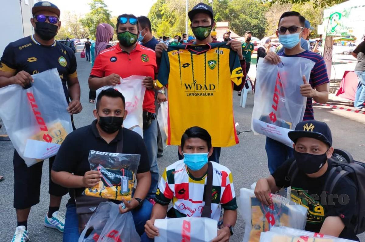 PEREKA logo KDA FC Ku Basri (tengah) dari Pendang memegang jersi hijau kuning musim 2021 yang baru dibelinya bersama penyokong Kedah di perkarangan Stadium Darul Aman. FOTO IZZALI ISMAIL