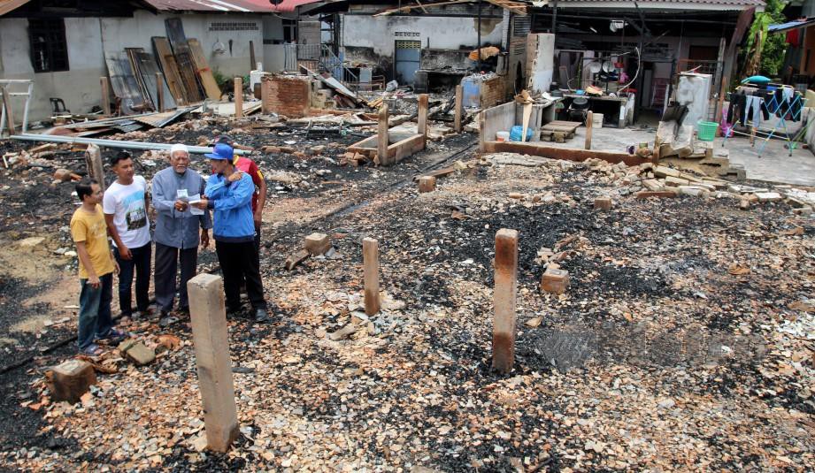 PEGAWAI Tenaga Nasional  Berhad (TNB) memeriksa kawasan kebakaran yang membabitkan 11 rumah selepas menyerah bil Penutupan akaun TNB di Kampung Padang Pohon Tanjong, Wakaf Bharu. FOTO Nik Abdullah Nik Omar