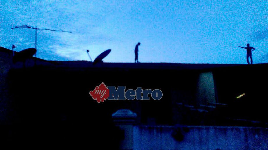 SUSPEK yang digelar angah mengacukan parang ke arah polis di atas bumbung rumah ketika melarikan diri di Taman Pulai Indah, Merlimau. FOTO NSTP/ IHSAN PEMBACA