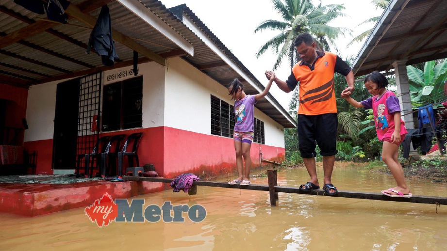 MOHAMAD Syafie Abdul Rahman, 42, bersama anaknya berjalan di atas titi kayu selepas kedainya Kampung Paloh Nyoir, Hulu Terengganu dilanda banjir. FOTO Ghazali Kori