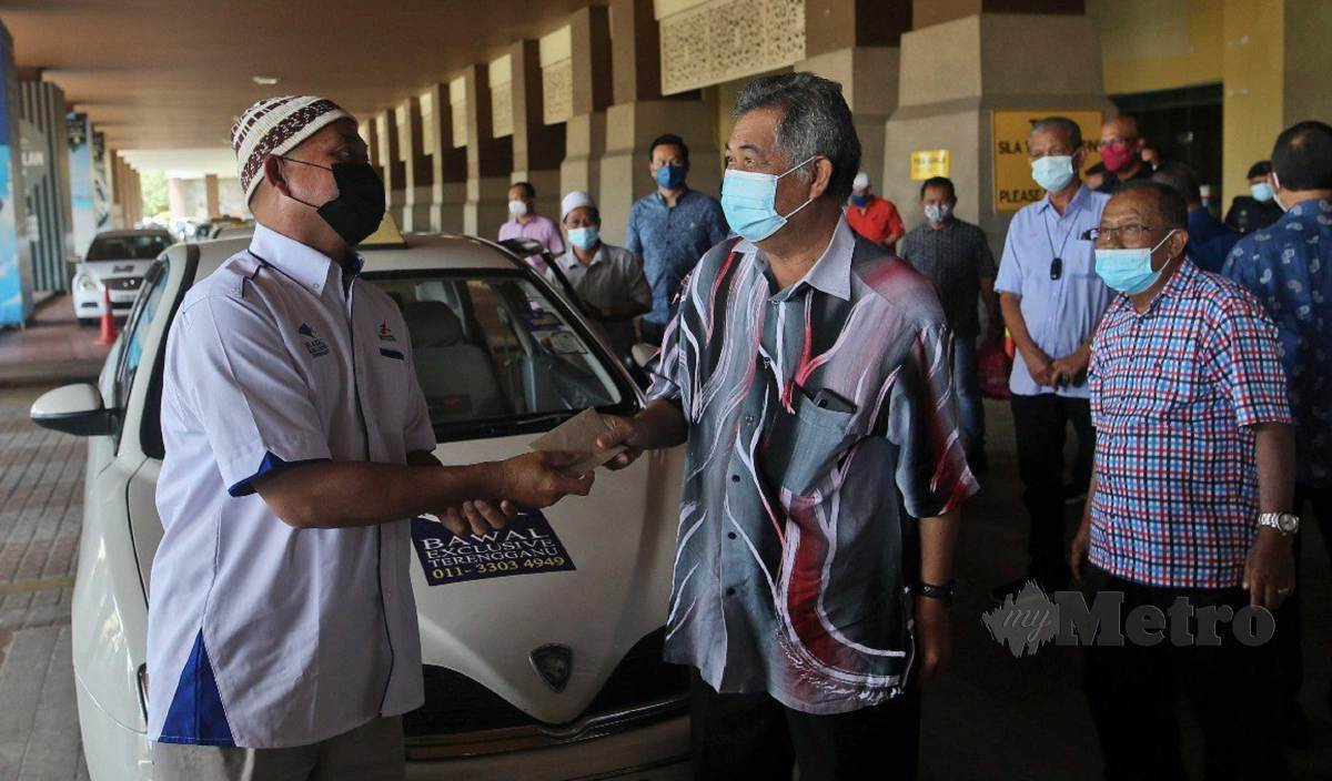 AHMAD Said (tengah) menyampaikan bantuan kepada pemandu kereta sewa Airport Secara Pandu Lalu di Lapangan Terbang Sultan Mahmud. FOTO Ghazali Kori