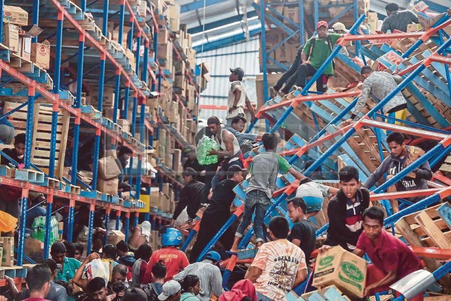 PENDUDUKAN tempatan membawa keluar makanan daripada gudang. FOTO/AFP  