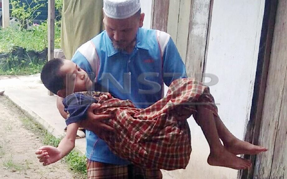 MOHD Ariff Ismail, 45, mendukung anaknya Muhammad Azwar, 11, masuk ke dalam rumah di Madrasah Ar Rahmaniah, Seberang Pekan selepas pulang dari rumah ibu saudaranya di Kampung Charuk Putih, Memali, Baling. FOTO Che Anisah Md Saad