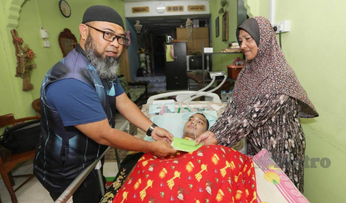 ASMADI (kiri) menyampaikan bantuan kewangan kepada Salbiah bagi pihak anaknya, Ahmad Fazlan yang mengalami lumpuh selepas saraf tunjangnya rosak. FOTO Mohd Rafi Mamat