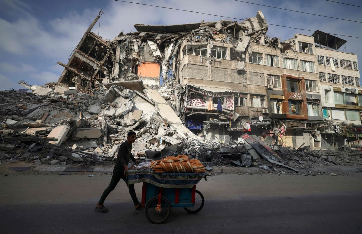 SEORANG penjual roti membawa barang jualannya melepasi runtuhan bangunan yang diserang rejim Zionis Israel. FOTO AFP