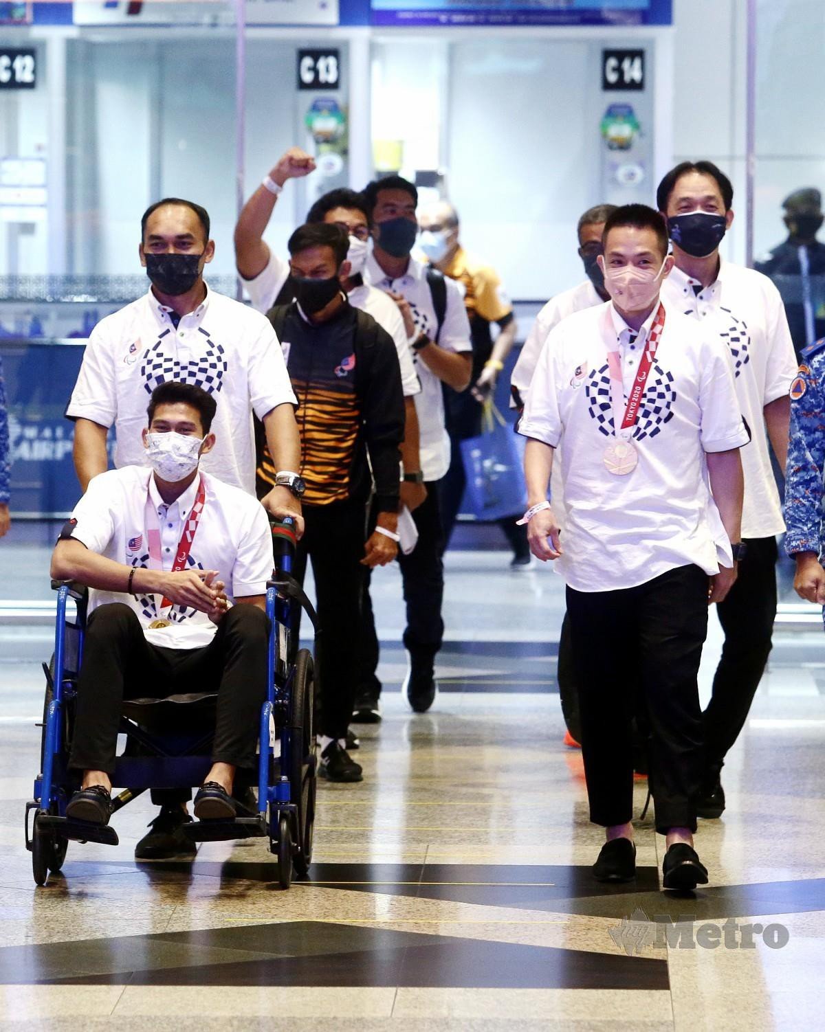 Atlet paralimpik Abdul Latif (bekerusi roda) dan Liek Hou (dua kanan) bersama jurulatih mereka selamat tiba di KLIA. FOTO Mohd Fadli Hamzah