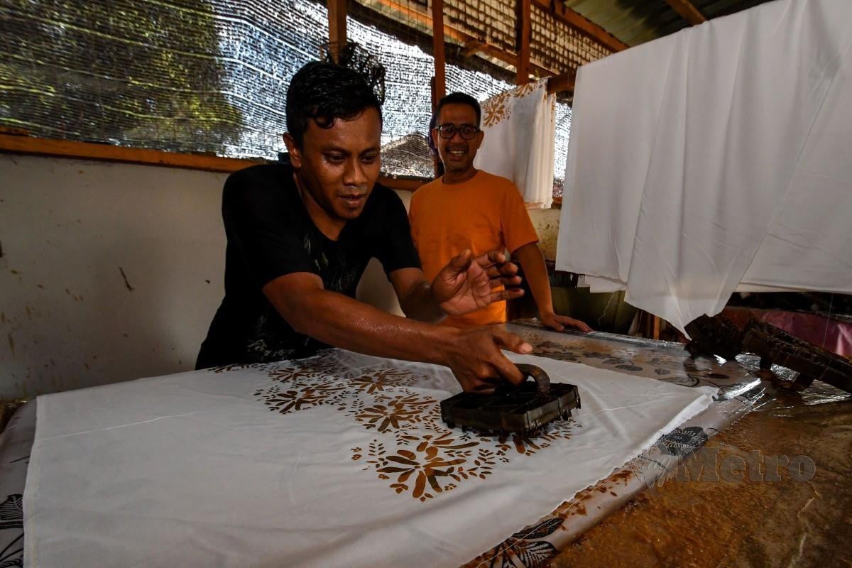 MOHD Nawawi (kanan) memantau pekerjanya melakukan proses menerap batik pada kain. FOTO Bernama 