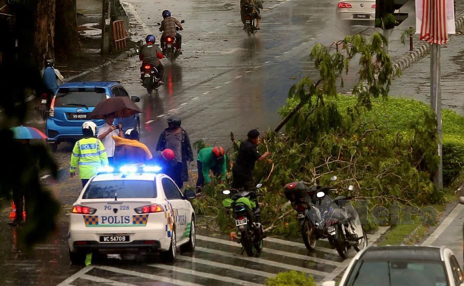 KAKITANGAN Majlis Bandaraya Pulau Pinang (MBPP) dibantu anggota polis mengalihkan pokok yang tumbang selepas kejadian ribut serta hujan lebat yang berlaku di Jalan Masjid Negeri. FOTO Danial Saad