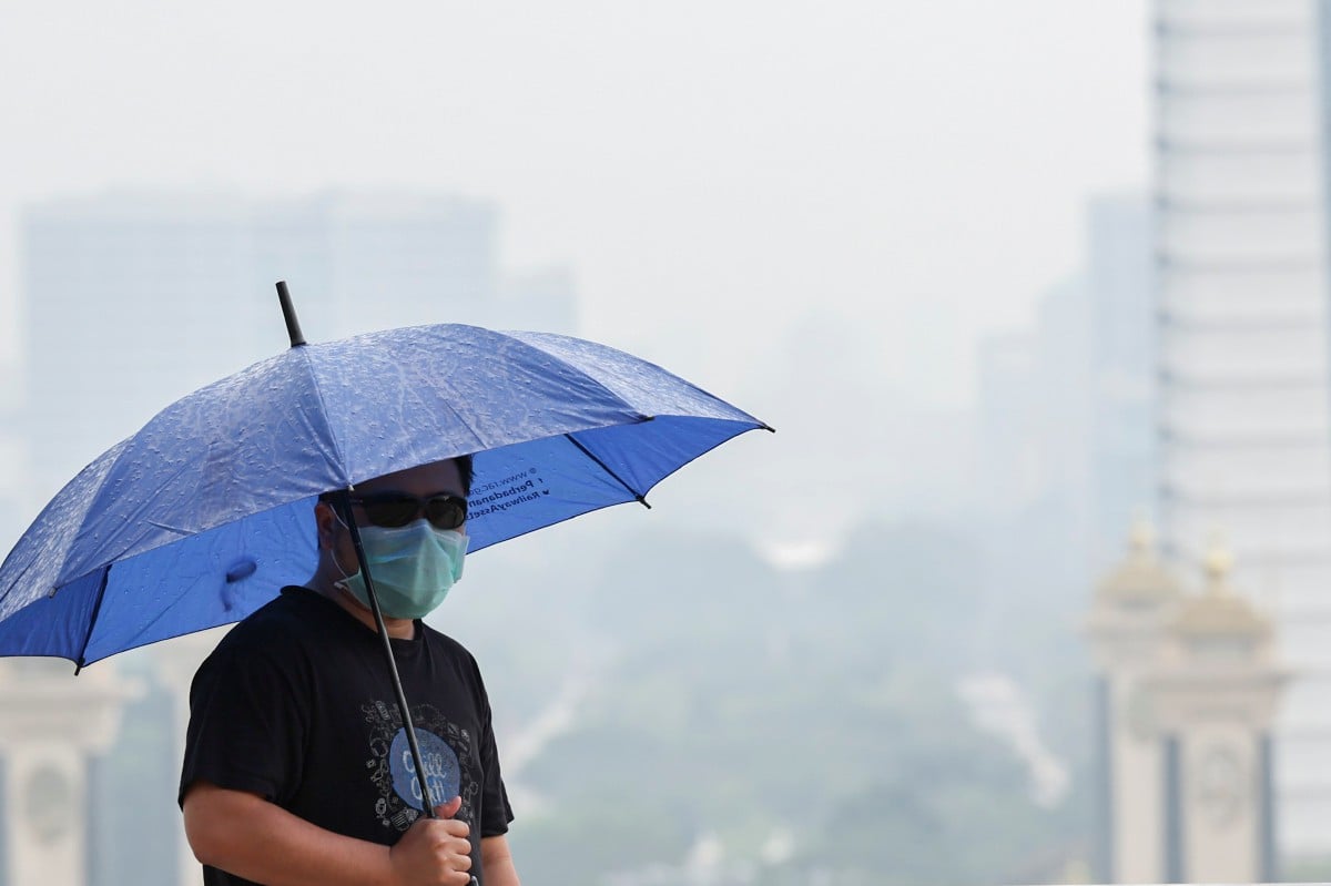 Seorang pemuda memakai pelitup muka dan berpayung ketika lalu di kawasan Pusat Pentadbiran Kerajaan di Putrajaya yang diselubungi jerebu disertai hujan renyai. FOTO BERNAMA