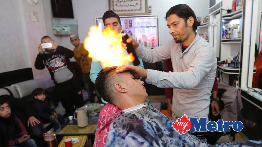 RAMADAN Odwan menyembur api untuk meluruskan rambut pelanggannya. FOTO Reuters