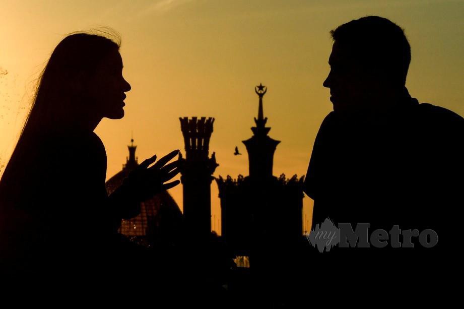 PASANGAN kekasih berbual ketika matahari terbenam di hadapan Druzhba Narodov, Rusia. FOTO AFP