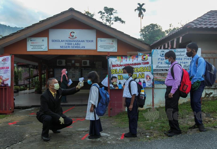 Guru Besar SK Tekir, Hisham Mohamed (kiri) memeriksa bacaan suhu badan pada  murid yang tiba ke sekolah. FOTO AZRUL EDHAM MOHD AMINUDDIN