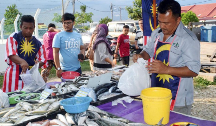 RAMDAN (kanan) membungkus ikan yang dijual di gerainya di Pasar Tani Banggol Indah.