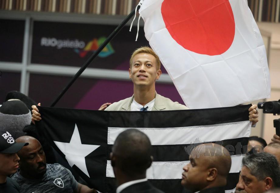 Keisuke Honda memegang bendera Botafogo ketika tiba di lapangan terbang. FOTO Reuters