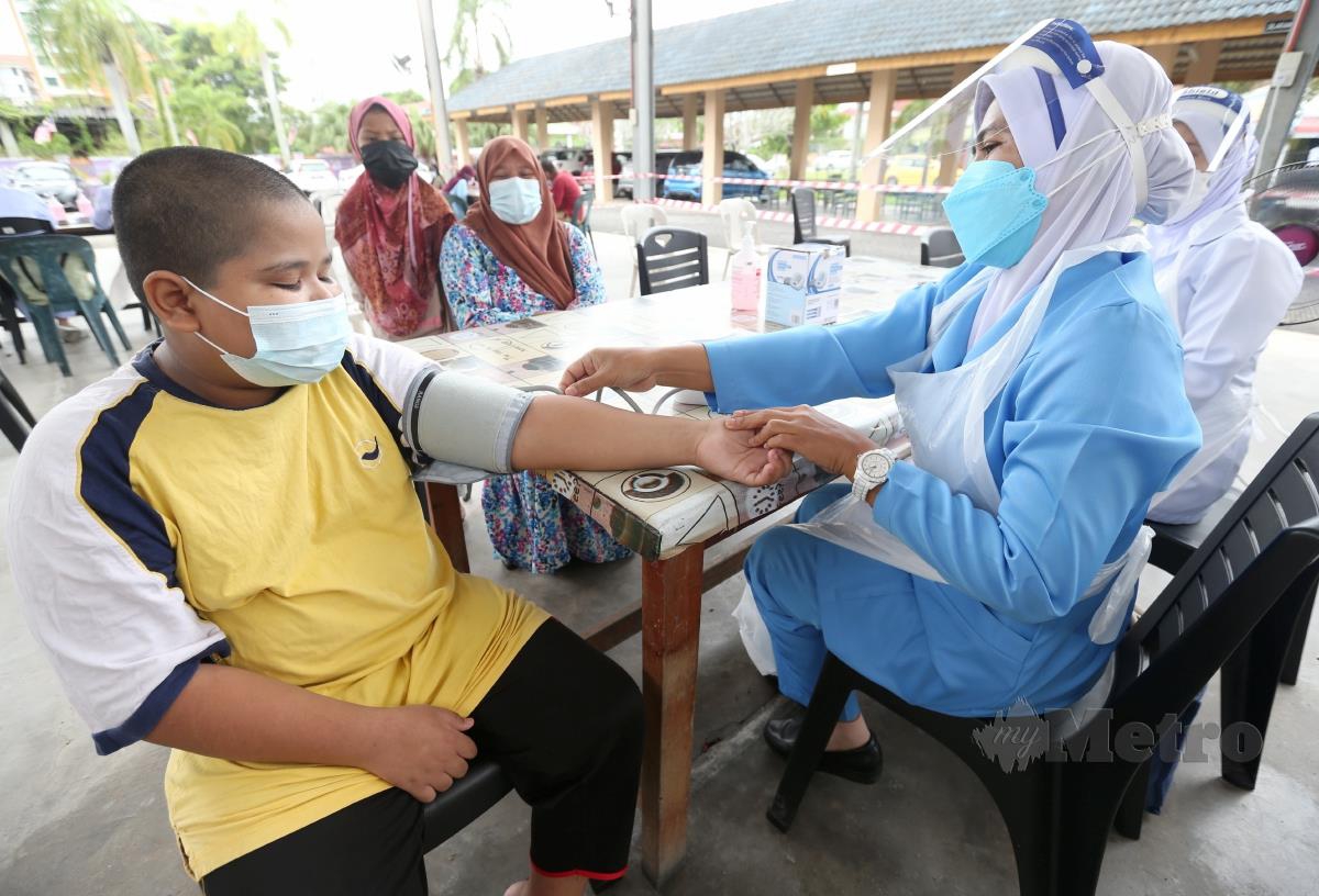 PETUGAS kesihatan memeriksa tekanan darah Mohd Amirul Asri, 12, sebelum mendapatkan suntikan vaksin Covid-19 di Pusat Pemberian Vaksin (PPV) Remaja  di Dewan Sekolah Kebangsaan Demit 2, Panji, semalam. FOTO NIK ABDULLAH NIK OMAR