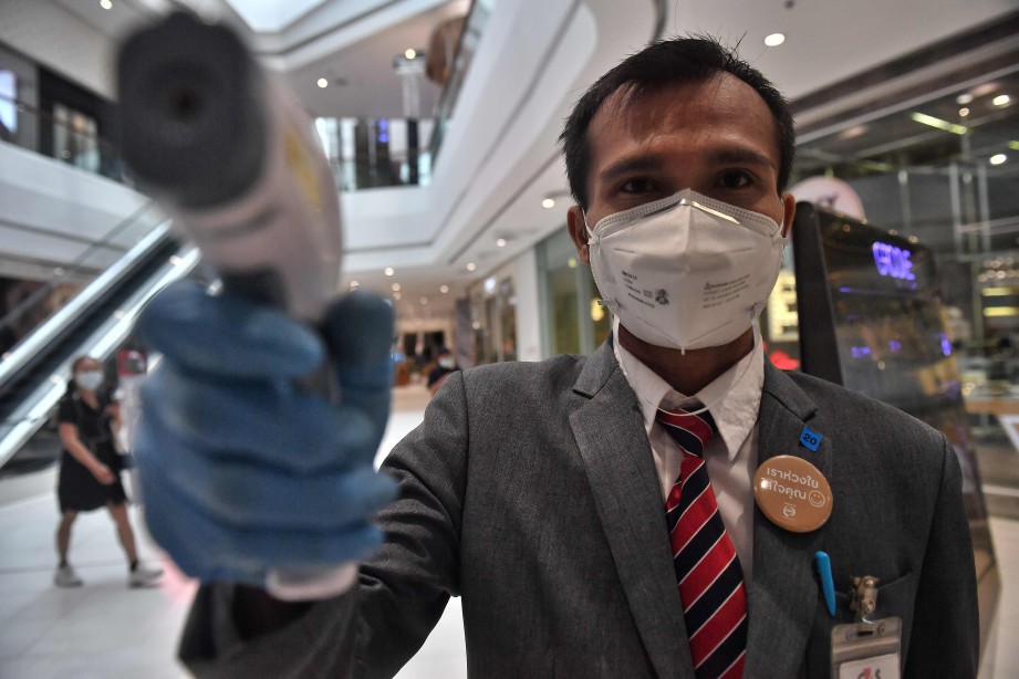 PENGAWAL keselamatan melakukan saringan suhu di pintu masuk pusat beli-belah di Bangkok. FOTO AFP 