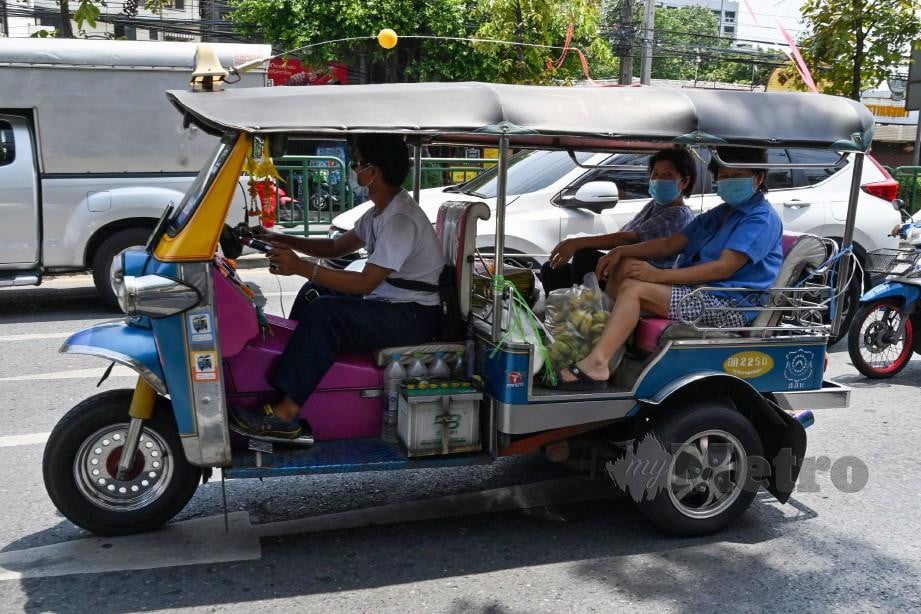 PEMANDU tuk tuk membawa penumpang dengan memakai penutup hidung dan mulut di sekitar Bangkok. FOTO AFP