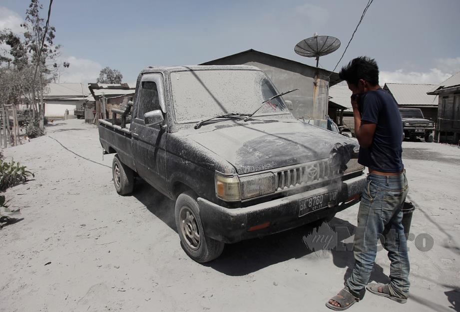 PENDUDUK membersihkan kenderaannya yang diliputi debu tebal kesan letusan Gunung Berapi Sinabung pada Isnin lalu. FOTO AFP