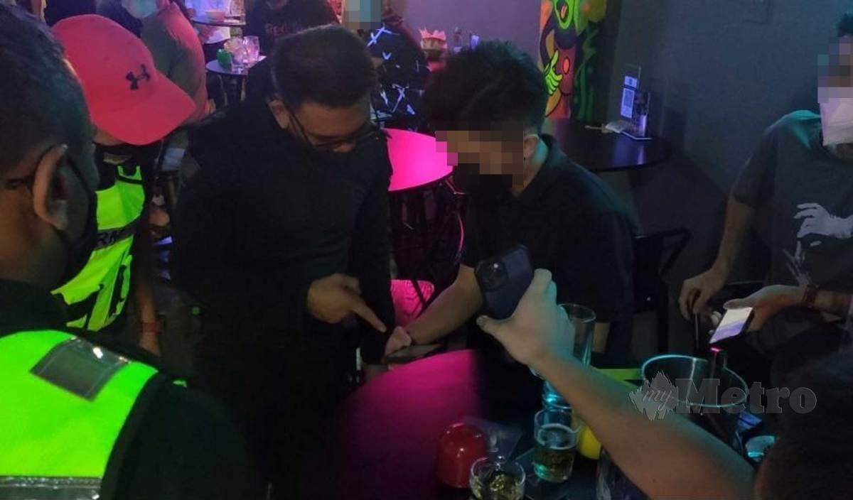 PEGAWAI polis dari IPK Kedah memeriksa sijil vaksin pada My Sejahtera remaja lelaki berusia 17 tahun yang belum mencapai tempoh matang 14 hari di sebuah pub yang diserbu di Sungai Petani. FOTO Zuliaty Zulkiffli
