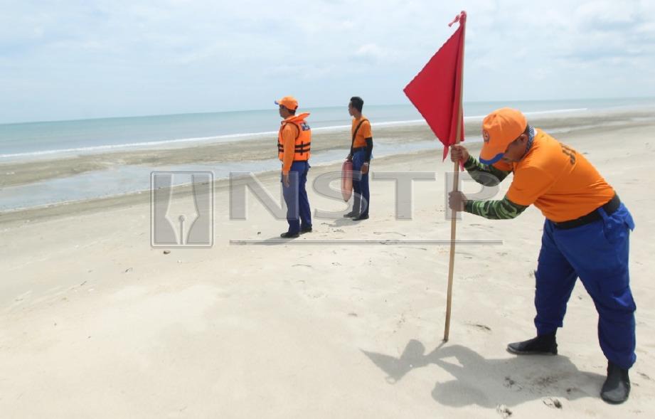 ANGGOTA Angkatan Pertahanan Awam Malaysia (APM) membawa bendera merah untuk dipacakkan bagi memastikan pengunjung tidak melakukan sebarang aktiviti mandi berikutan laut bergelora dan ombak besar musim tengkujuh.  FOTO Muhd Asyraf Sawal