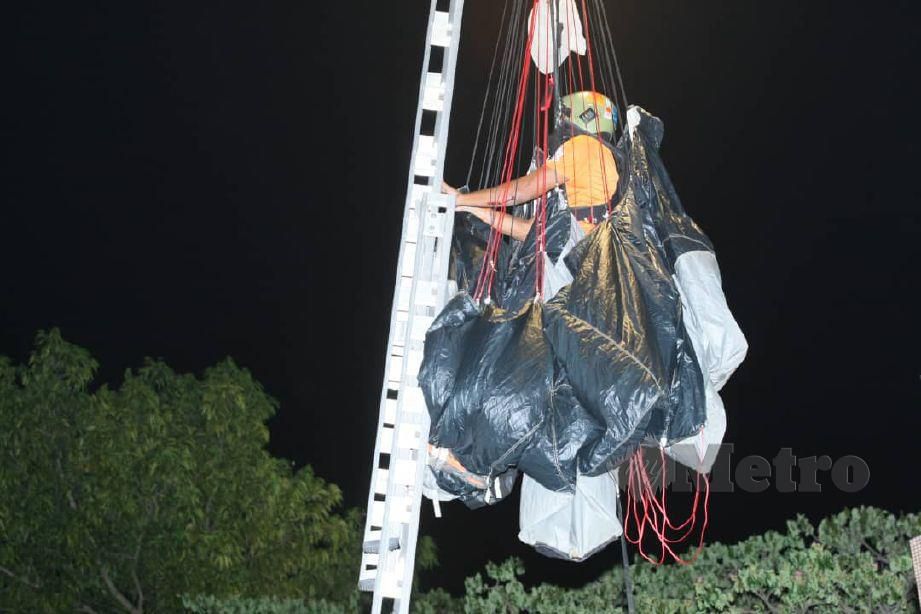 PESERTA terjunan ekstrem 'Taming Sari Tower Base Jump' tersangkut pada tiang lampu diselamatkan oleh Anggota Bomba dan Penyelamat di hadapan Menara Taming Sari, Banda Hilir. FOTO Khairunisah Lokman