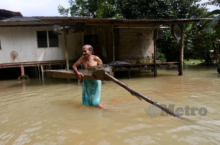 KAMARUDDIN mengalihkan kayu yang hanyut di hadapan rumahnya akibat banjir. FOTO Ghazali Kori