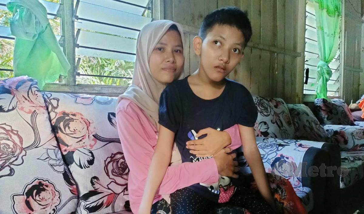 SITI Fatihah memangku Puteri Airin Amani yang tidak dapat berjalan dan bercakap kerana kerap diserang sawan ketika bayi ketika ditemui di rumahnya di Kampung Hulu Geh. FOTO Siti Rohana Idris
