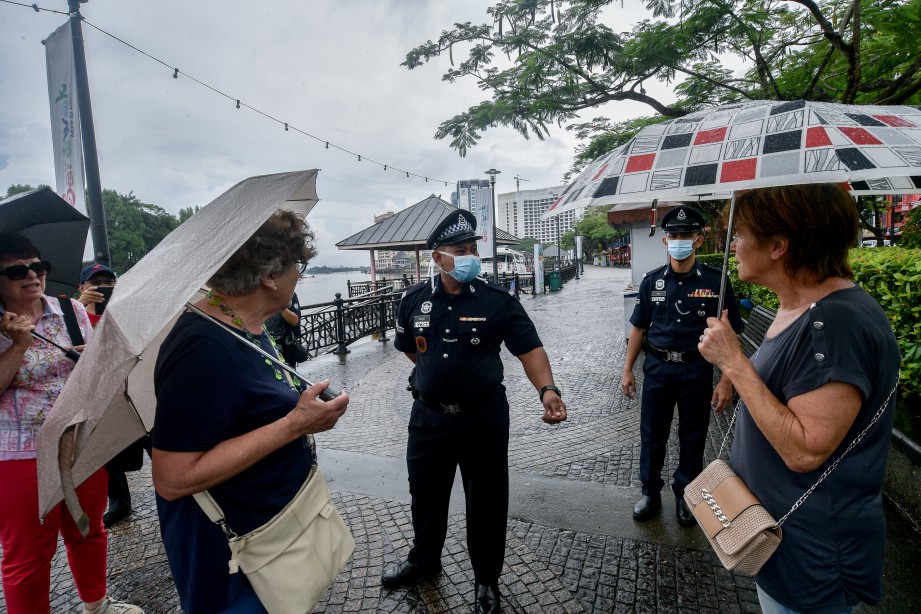ANGGOTA polis memberi penerangan kepada beberapa orang pelancong di Tebingan Sungai Kuching susulan Perintah Kawalan Pergerakan. FOTO BERNAMA