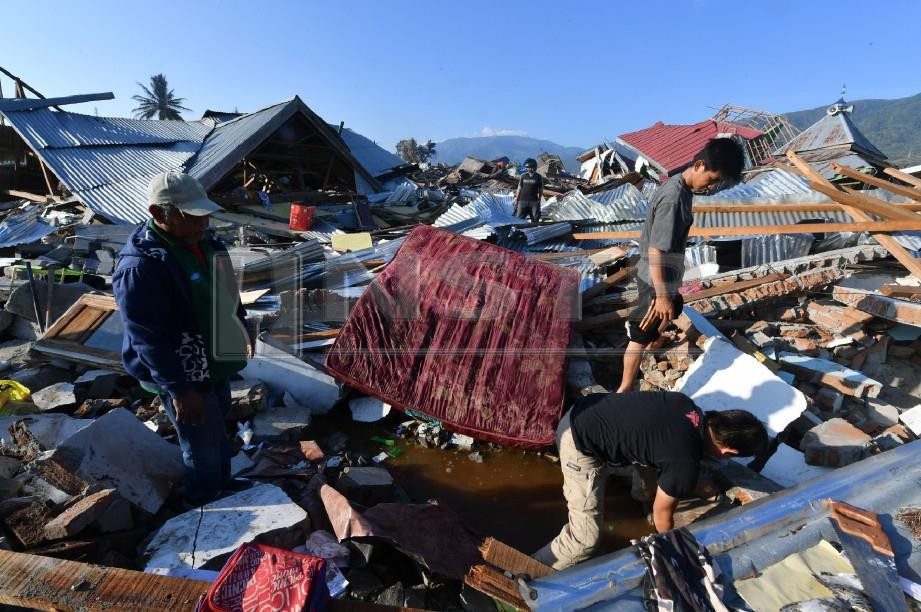 ANTARA mangsa yang terselamat cuba mencari keluarganya di runtuhan rumah mereka di kampung Balaroa, Palu. -Foto AFP