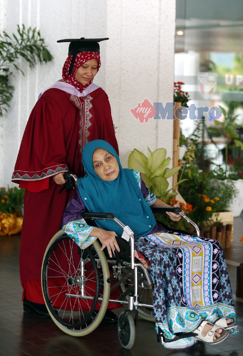 Graduan Sarjana Muda Sains (Sains Bioperubatan), Anis Ayuni Ismail menolak kerusi roda  ibunya, Nik Mah Nik Kob, 62, ketika majlis  Konvokesyen UPM Ke-40, hari ini. - Foto SURIANIE MOHD HANIF