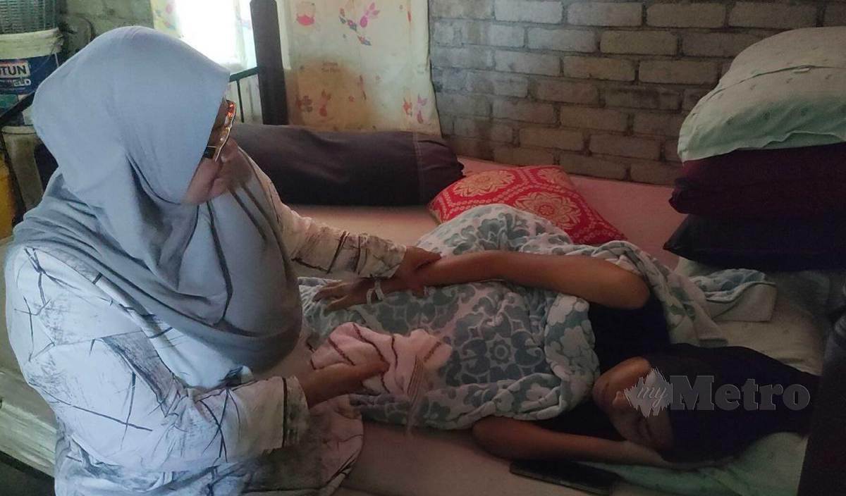 SARUNAM mengelap tangan anaknya, Nur Ayu Mas Aiza yang menghidap kanser buah pinggang tahap empat di rumah mereka di Kampung Alor Sekawan, Mukim Tajar. FOTO Zuliaty Zulkiffli