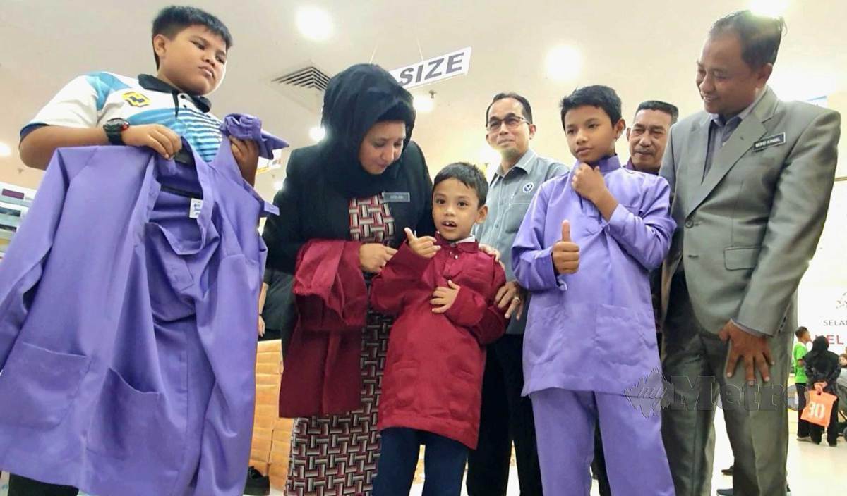 HASLINA (dua dari kiri) membantu anak yatim piatu, Muhammad Raizill Darwish (tiga dari kiri) mencuba baju Melayu baharu pada Program Sinaran Kasih anjuran Langkawi Port di Langkawi Fair, Langkawi. FOTO Hamzah Osman