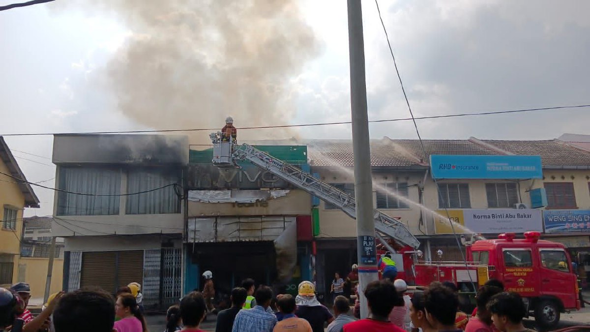 ANGGOTA bomba memadamkan kebakaran kedai telefon yang berpunca daripada unsur khianat. FOTO Ihsan PDRM.