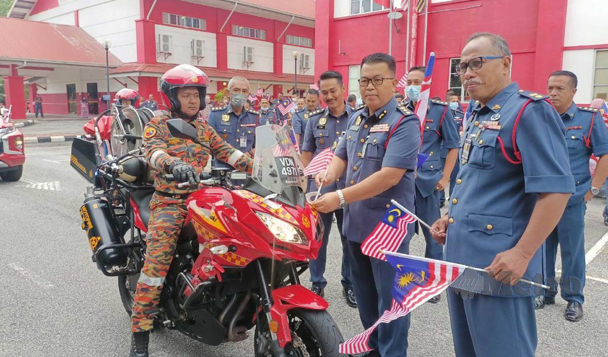 ZAINAL (tengah) meletakkan Jalur Gemilang di motosikal yang digunakan oleh anggota dari Unit Rondaan Bermotosikal (URB) JBPM Kelantan sempena gimik pelancaran Bulan Kebangsaan di Dataran Dato' Hj Soiman, Tunjong. FOTO Siti Rohana Idris