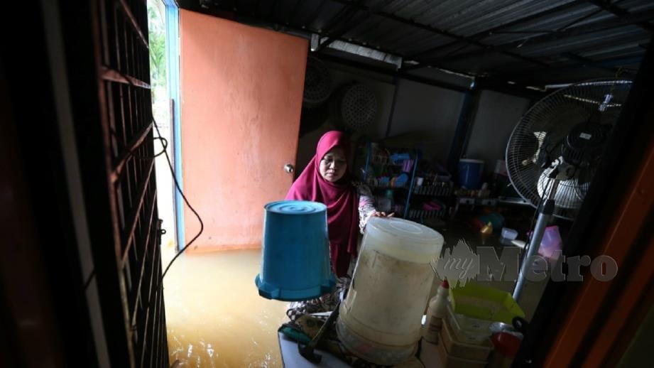 HASSIMAH Hassim, 53, menyelamatkan perkakas dapur yang ditenggelami air akibat hujan lebat dan fenomena air pasang besar, di Kampung Parit Mahang, Kuala Selangor. FOTO Saddam Yusoff.