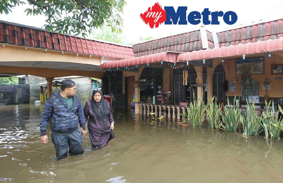 Siti Ajarah bersama anaknya meredah air banjir yang menenggelami ruang dalam dan luar rumahnya di Kampong Tanjung Pauh, hari ini. FOTO Sharul Hafiz Zam