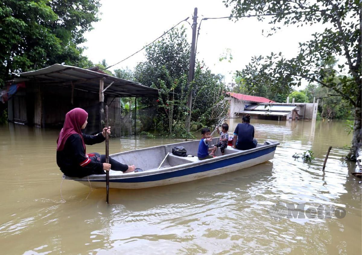 Siti Nor Ayuni Che Omar bersama kakaknya, Siti Nur Ilahie Che Omar menggunakan bot untuk membeli keperluan harian mereka susulan jalan utama Pekan Rantau Panjang sudah mulai surut, hanya beberapa kampung sahaja yang masih digenangi air  di Kampung Tersang  di sini. FOTO NIK ABDULLAH NIK OMAR