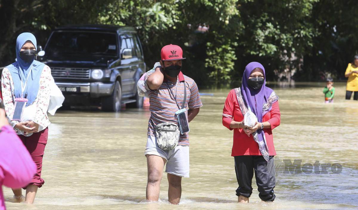 SEBAHAGIAN penduduk Kampung Tersang meredah air banjir untuk berpindah ke PPS. FOTO Nik Abdullah Nik Omar