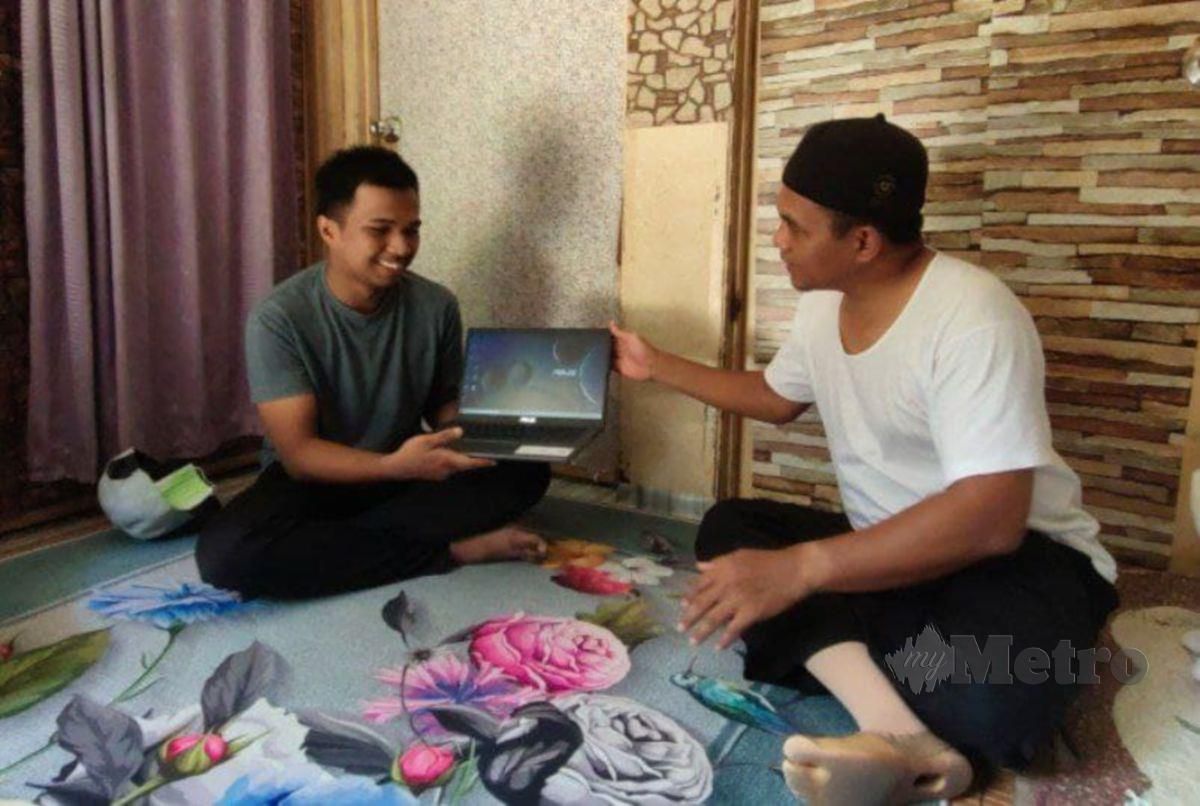 Mohd Zuraidi (kiri) menerima sumbangan komputer riba daripada Raja Shamri di rumahnya di Kampung Changgal. FOTO SYAHERAH MUSTAFA