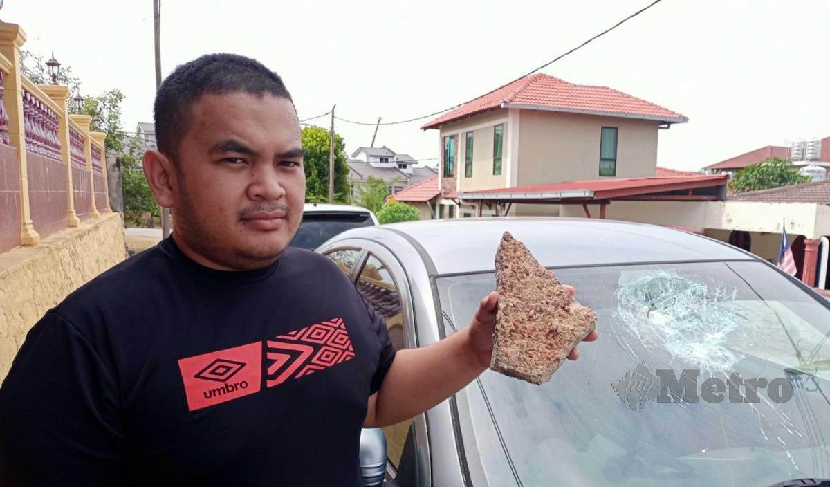 MUHAMMAD Syahir menunjukkan keadaan cermin kereta yang pecah dan batu yang digunakan oleh pelaku di depan rumahnya di Taman Datuk Abdul Samad, Port Dickson. FOTOMohd Khidir Zakaria